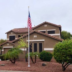 aluminum flagpole with American flag in front of brown and white home with stone yard